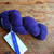 Malabrigo Worsted Violetas purple hand-dyed merino wool yarn skein with tag on rustic wood background, showcasing vibrant color and textured fiber.