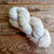 Malabrigo Worsted Simple Taupe skein of neutral hand-dyed merino yarn, soft grayish-beige color, twisted into a loop on a wooden surface.