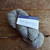 Malabrigo Worsted Pearl yarn, soft white merino wool skein, labeled as 036 Pearl, on a wooden surface, showcasing its gentle gray-white hue.