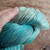 Malabrigo Rios yarn, Celestina color, Superwash Merino Worsted yarn skein, turquoise blue green hues, held in a hand on wooden background.