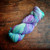 Malabrigo Rios RIO-266 Melissa Superwash Merino Worsted Yarn skein in purple, blue, and green hues on a wooden surface.