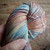 Malabrigo Rios Zahara Superwash Merino Worsted Yarn, multicolored with shades of blue, orange, pink, and gray, skein in hand.
