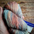 Malabrigo Rios RIO-267 Zahara Superwash Merino Worsted Yarn, multicolored yarn with shades of pink, blue, and orange, skein in hand.