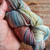 Malabrigo Rios Zahara Superwash Merino Worsted Yarn, multicolored skein with shades of blue, red, yellow, and gray, held in a hand.