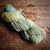 Malabrigo Rios yarn, Gardenia color, Superwash Merino Worsted skein, green, beige, and blue hues, on a wooden surface, showcasing soft, chunky texture.
