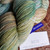 Malabrigo Rios yarn, Gardenia color, Superwash Merino Worsted yarn skein with label and tag, showcasing soft green, blue and beige hues.