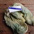 Malabrigo Rios yarn, Gardenia color, Superwash Merino Worsted skein, soft yellow and green hues, white label, on a wooden surface.