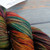 Multicolored merino yarn skein, Malabrigo Rios Sagittarius, muted rainbow hues, showcasing earthy tones of green, orange, red, and brown in twisted bundle.