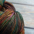 Malabrigo Rios Sagittarius yarn, muted rainbow merino wool skein in earthy tones of green, orange, brown, and pink, showcasing colorful texture.