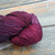 Malabrigo Rios Purpuras yarn, a berry purple superwash merino wool skein from Malabrigo, showcasing a rich, deep purple hue with subtle color variations, neatly coiled on a wooden surface. Malabrigo Rios Purpuras yarn, a berry purple superwash merino wool skein from Malabrigo, showcasing a rich, deep purple hue with subtle color variations, neatly coiled on a wooden surface.