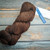 Malabrigo Rios Coco Tonal Espresso Superwash Merino Yarn skein in rich brown color with tag on rustic wooden background.
