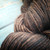Malabrigo Rios Coco Tonal Espresso Superwash Merino Yarn, brown and black hues intertwined, soft yarn skein on a light blue background.