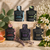 Eucalan Delicate Wash Pods in various scents, five black boxes with colorful designs on a stone display surrounded by flowers and fruits.