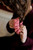 Woman's hands securing brown hair with a pink knitted scrunchie, wearing a maroon sweater. Pattern from 52 Weeks of Accessories by Laine Publishing.