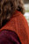 Close-up of rust-colored knitted vest with intricate patterns on upper back, worn by person with long brown hair, Laine Publishing accessory.