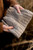 Person holding folded light grey knitted fabric with intricate patterns, pattern from Laine Publishing's 52 Weeks of Accessories collection.