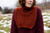 Woman wearing maroon sweater and rust-colored knitted scarf-neck warmer, Laine Publishing 52 Weeks of Accessories pattern, in a snowy outdoor setting.