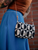Black and white patterned crossbody bag with brown strap, hanging from a woman's waist beside a brick wall, showcasing stylish accessory details.