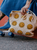 Beige tote bag with yellow smiley faces, blue skateboard and shoes, and blue denim skirt on a grey and orange surface.