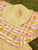 Crochet blanket with pink, orange, and white check pattern, fringed edges, and a straw hat on top, for home and life decor.