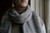 Gray and white knitted scarf with striped pattern wrapped around neck, worn by person with taupe turtleneck, showcasing texture and weave up close.