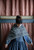 Woman wearing blue dress and white patterned shawl, draped over shoulders,
