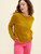 Woman wearing mustard yellow knit sweater and pink pants, posing with hands in pockets, showcasing casual fashion style and comfortable clothing.