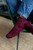 Burgundy knitted socks on a person's feet, showcasing a textured pattern, worn with blue jeans and resting on a green chair.