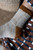 Brown, beige, and white knitted sock with brown stripes on cuff, on a leg wearing a brown, navy, and white striped skirt.