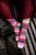 Woman's feet wearing colorful patterned socks with white toes, sitting on wooden bench, showcasing vibrant pink, orange, blue, and red knitted footwear.