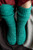 Teal knitted socks with ribbed texture and folded cuffs on a person's feet against a gray and red background, 52 Weeks of Socks Vol II.