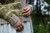 Woman wearing green and beige colourwork knitted sweater, light blue skirt with white pattern, hands in front, outdoors in natural setting.