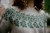 Strands of Joy knitting pattern, green floral design on a light grey sweater, showcasing colourwork technique for a calm and cozy look.
