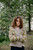 Woman wearing green and beige floral patterned sweater with arms crossed standing in front of trees, showcasing Strands of Joy knitting pattern.