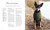 Olive green dog sweater on a black and brown dog outdoors beside a path with a body of water in the background.