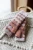 Knitted fingerless gloves in orange, brown, and grey stripes, made from soft yarn, resting on a cream-colored woven fabric with a handle.