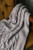 Light gray knitted blanket with cable pattern draped over mustard yellow armchair, showcasing textured weave and soft folds.