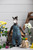 Mouche & Friends donkey plush toy wearing blue overalls stands beside a basket with flowers and a knitted chicken, by Laine Publishing.