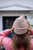 Woman wearing light brown knitted beanie from Knits to Wear: Effortless Patterns by Kutova Kika, Laine Publishing, with pink sweater outdoors.
