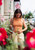 Woman wearing orange halter top and beige pants standing amidst pink flowers, holding sunglasses, showcasing effortless summer fashion with Laine Publishing's Knits to Wear.