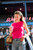 Woman wearing pink sleeveless top, blue jeans, and carrying tan purse, holding drink in a casual setting with neon signs.