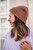 Woman wearing a brown beanie and light purple knit sweater from Knits to Wear: Effortless Patterns by Kutova Kika from Laine Publishing.