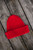 Red ribbed knit beanie by Laine Publishing, from Knits to Wear: Effortless Patterns by Kutova Kika, displayed on rustic wooden planks.