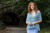 Woman with curly red hair wearing blue patterned Malabrigo Verano top and light blue skirt standing outdoors in front of a tunnel.