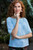 Woman wearing light blue Malabrigo Verano Pima cotton top with floral bottoms, posing outdoors with thoughtful expression.