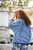 Woman with long red hair wearing blue and white stripped top and floral pants standing outdoors in front of a building.