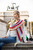 Woman wearing white shirt and jeans with colorful striped scarf, Malabrigo Verano Pima Cotton Collection, sitting outdoors in front of arch.