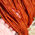 Strands of handspun yarn held in hand to show orange tonal coloration.