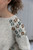White knitted sweater with brown and green floral embroidery on the shoulder and arm, made using scrap yarn for crochet patterns.