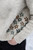 Cream-colored sweater with brown and green floral pattern, worn by a person with hand in pocket, made from knitted or crocheted yarn.